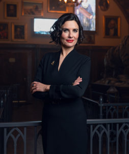 Photograph of the President of the Adventure Club of Europe, Catherine Noir. She has short black hair and stands with her arms crossed over her chest.